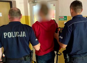 zatrzymany mężczyzna jest prowadzony przez 2 policjantów korytarzem budynku