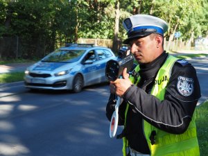 policjant stoi przy drodze i trzyma w ręce fotoradar