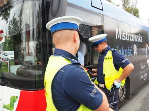 policjant sprawdza stan trzeźwości kierującego autobusem stojąc przy otwartej szybie autobusu