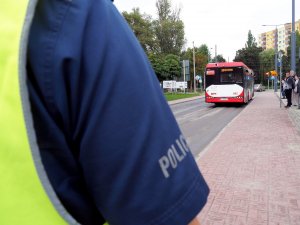 rękaw koszuli od munduru z napisem policja, w tle autobus