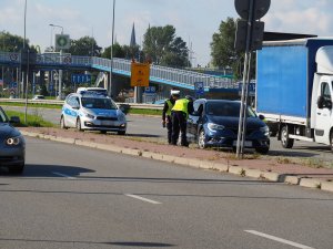 dwóch policjantów przy drodze rozmawia z kierowcą niebieskiego samochodu przez otwarta szybę