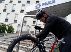 pracownik sklepu zapina rower zabezpieczeniem do barierki przy schodach przed Komendą Miejską Policji w Częstochowie