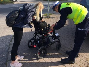policjant z kobieta pochylają się nad wózkiem - policjant przekazuje opaskę odblaskową dziecku, które siedzi w wózku