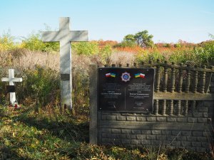 wejście na cmentarz w Kisielinie przed wykonaniem prac porządkowych - widać porośnięte roślinnością krzyże, na ogrodzeniu wisi tablica upamiętniająca objęcie patronatem NSZZP województwa śląskiego mogiły policjanta