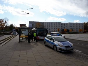 2 policjantów i 2 strażników miejskich stoi na przystanku, w oddali widać jadący autobus