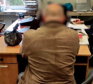 zatrzymany mężczyzna siedzi na krześle przodem do biurka na komisariacie