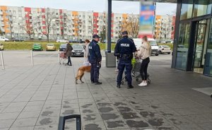 dwóch policjantów z psem służbowym rozmawia z kobietą przed wejściem do sklepu