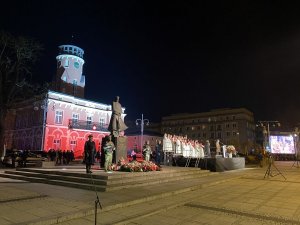 ratusz podświetlony na biały i czerwony kolor, na pierwszym planie pomnik Józefa Piłsudskiego z wartą honorową po dwóch stronach