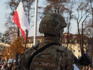 na pierwszym planie żołnierz w wojskowym mundurze, w tle flaga Polski