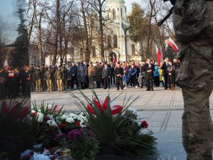 na pierwszym planie kwiaty pod pomnikiem, w tle służby mundurowe ustawione na Placu Biegańskiego
