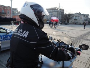 policjant na motocyklu, w tle flaga Polski wyświetlona na dużym ekranie