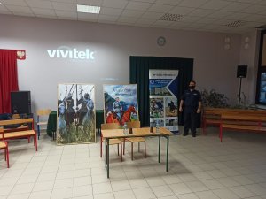 policjant w mundurze pozuje na tle bannerów promujących akcję