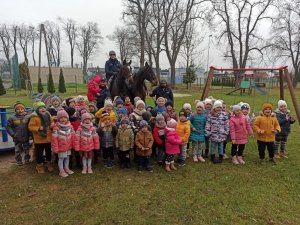 2 policjantów na koniach pozuje do zdjęcia z grupą przedszkolaków