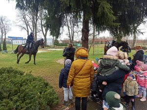 policjant na koniu prezentuje umiejętności swojego wierzchowca - przygląda mu się grupa przedszkolaków z opiekunami