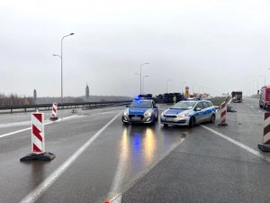 policyjny radiowóz zabezpiecza miejsce wypadku na autostradzie, w tle przewrócona cysterna