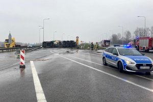policyjny radiowóz zabezpiecza miejsce wypadku na autostradzie, w tle przewrócona cysterna