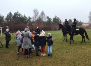 policjanci na koniach służbowych prezentują umiejętności wierzchowców przyglądającej się im grupie dzieci