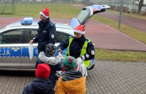 policjantka w czapce Mikołaja rozdaje dzieciom prezenty przy radiowozie