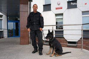 policjant z psem słuzbowym pozują na tle komendy