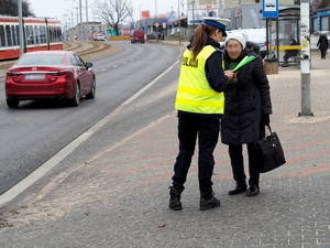 policjantka w kamizelce odblaskowej przekazuje opaski odblaskowe pieszym na chodniku