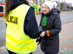 policjantka w kamizelce odblaskowej przekazuje opaski odblaskowe pieszym na chodniku