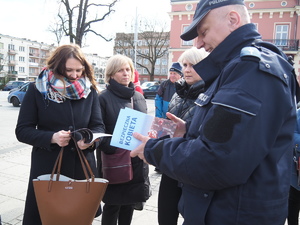 policjant wręcza poradnik stojącym na Placu Biegańskiego kobietom