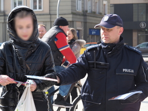 policjant wręcza kobiecie poradnik na Placu Biegańskiego