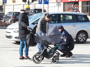 policjant kuca przy wózku, obok stoi mężczyzna i kobieta