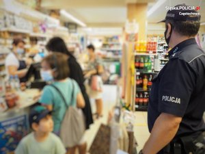 policjant w sklepie patrzy w stronę kasy, przy której stoją klienci