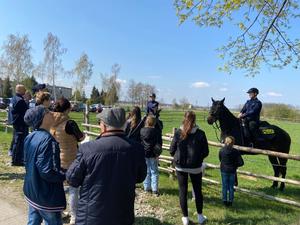 policjanci na koniach stoją na trawie, przed nimi grupa osób przygląda się im