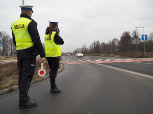 policjant z tarczą do zatrzymywania pojazdów i policjantka z ręcznym miernikiem prędkości stoją przy drodze