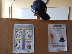 tablica korkowa, przywieszone na niej plakaty z konkursu - na górze powieszona czapka policyjna