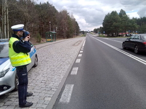 policjant z ręcznym miernikiem prędkości w dłoni mierzy prędkość przejeżdżających samochodów