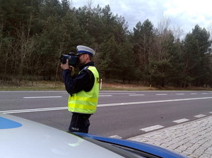 policjant z ręcznym miernikiem prędkości w dłoni mierzy prędkość przejeżdżających samochodów