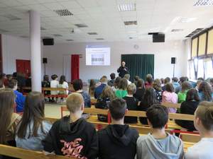 policjanci w mundurach prowadzą pogadankę dla uczniów w sali lekcyjnej - uczniowie siedzą w ławkach tyłem do fotografującego