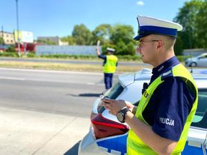 2 policjantów stoi przy radiowozie, w tle 2 pasy ruchu