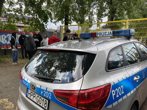 na tle radiowozu kibice idący na mecz piłkarski przed wejściem na stadion