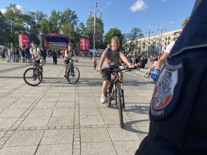 na pierwszym pl;anie policyjna naszywka na mundurze - zbliżenie, w tle nadjeżdżająca grupa kilku chłopców na rowerach