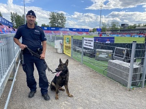 policjant z psem służbowym pozują do zdjęcia na tle trybun stadionu piłkarskiego