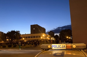 napis policja na dachu radiowozu, w tle studenci na imprezie plenerowej