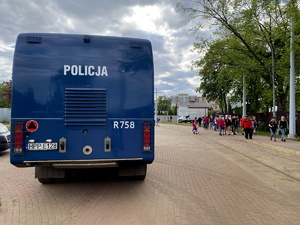 policyjny samochód - tak zwana armatka wodna zaparkowany przy stadionie, w tle kibice idą na mecz