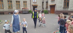 policjantka prowadzi za rękę przedszkolaka i szeroko uśmiecha się