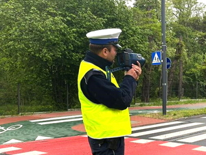 policjant mierzy prędkość pojazdom ręcznym miernikiem prędkości na przejściu dla pieszych