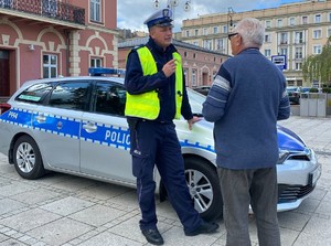 policjant rozmawia ze starszym mężczyzną przy radiowozie