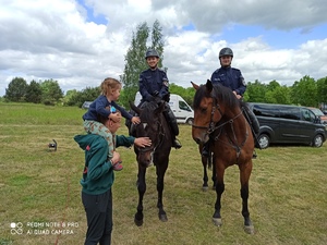 przy dwóch policjantach na koniach stoi rodzic z dzieckiem, głaskają konia