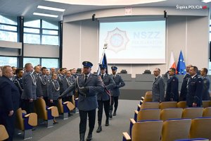 policjanci niosą sztandar i wychodzą z auli, w tle uczestnicy spotkania