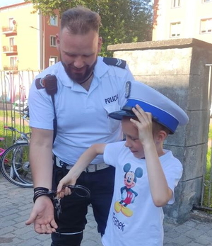 mały chłopczyk w czapce policyjnej zakłada kajdanki policjantowi