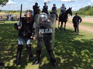 2 uczennice pozują do zdjęcia ubrane w sprzęt policyjny, za nimi 4 policjantów na koniach - uśmiechają się do siebie