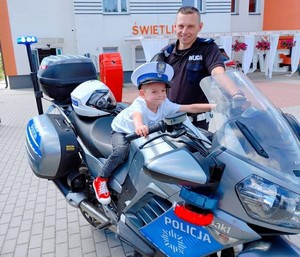 policjant przy motocyklu uśmiecha się, na motocyklu siedzi chłopczyk