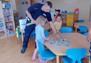 policjant kładzie na stoliku odblaski - przy stoliku siedzą przedszkolaki